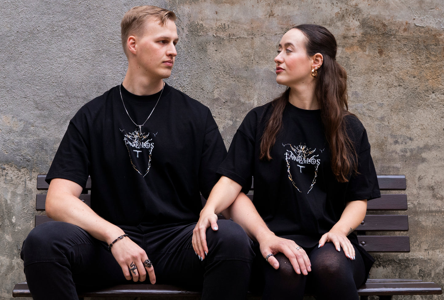 Two people sitting on a bench wearing black techno t-shirts with a logo 'TANTALOS'