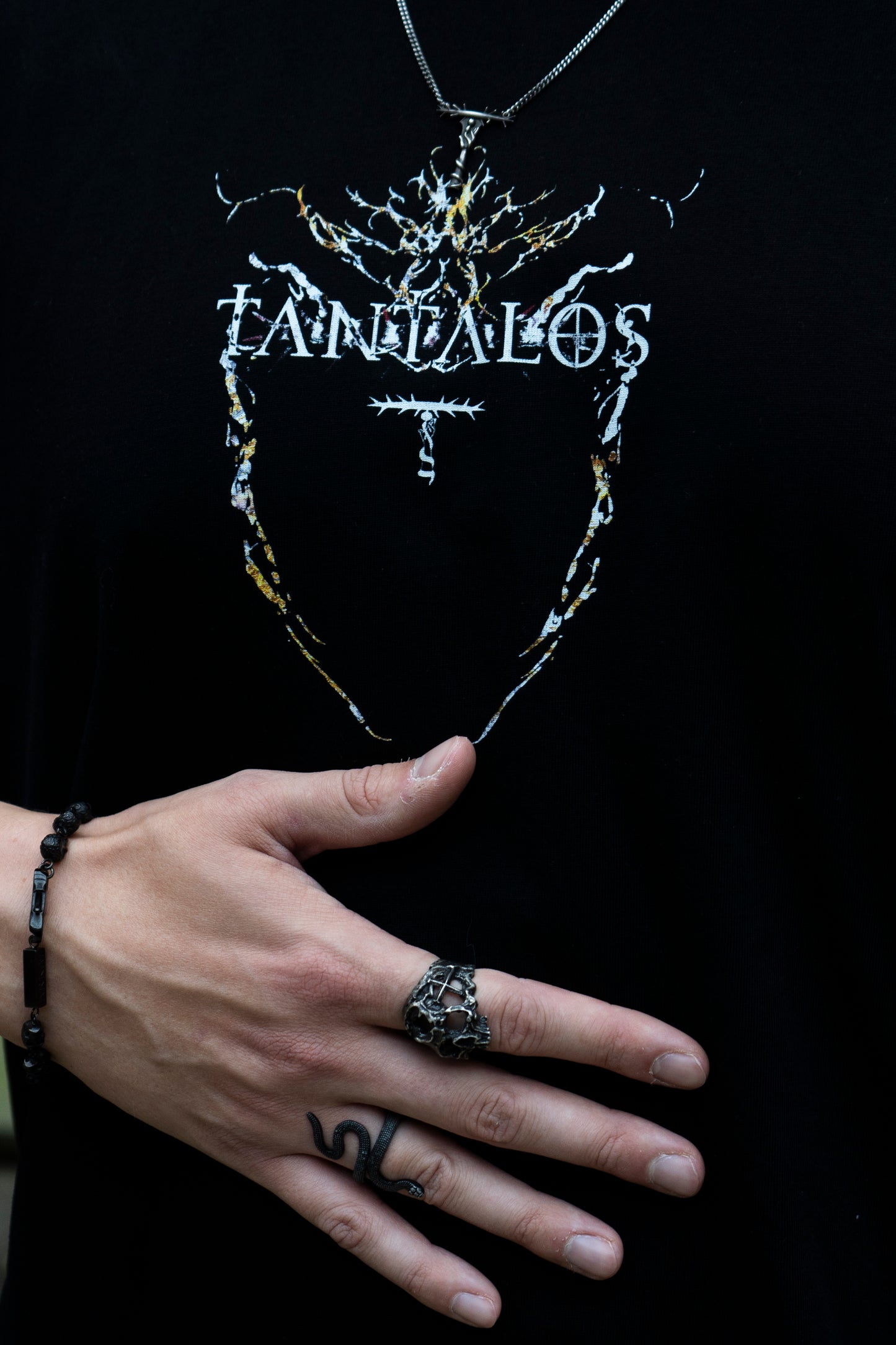 Hand with a ring holding a necklace with  a Techno T-shirt written 'Tantalos' on