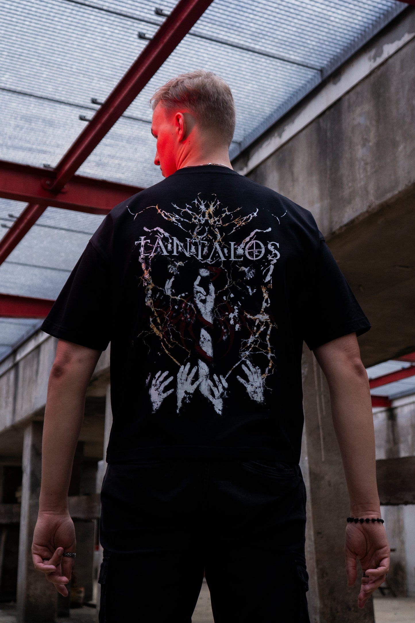 Person wearing a graphic TANTALOS techno T-shirt, in an industrial setting