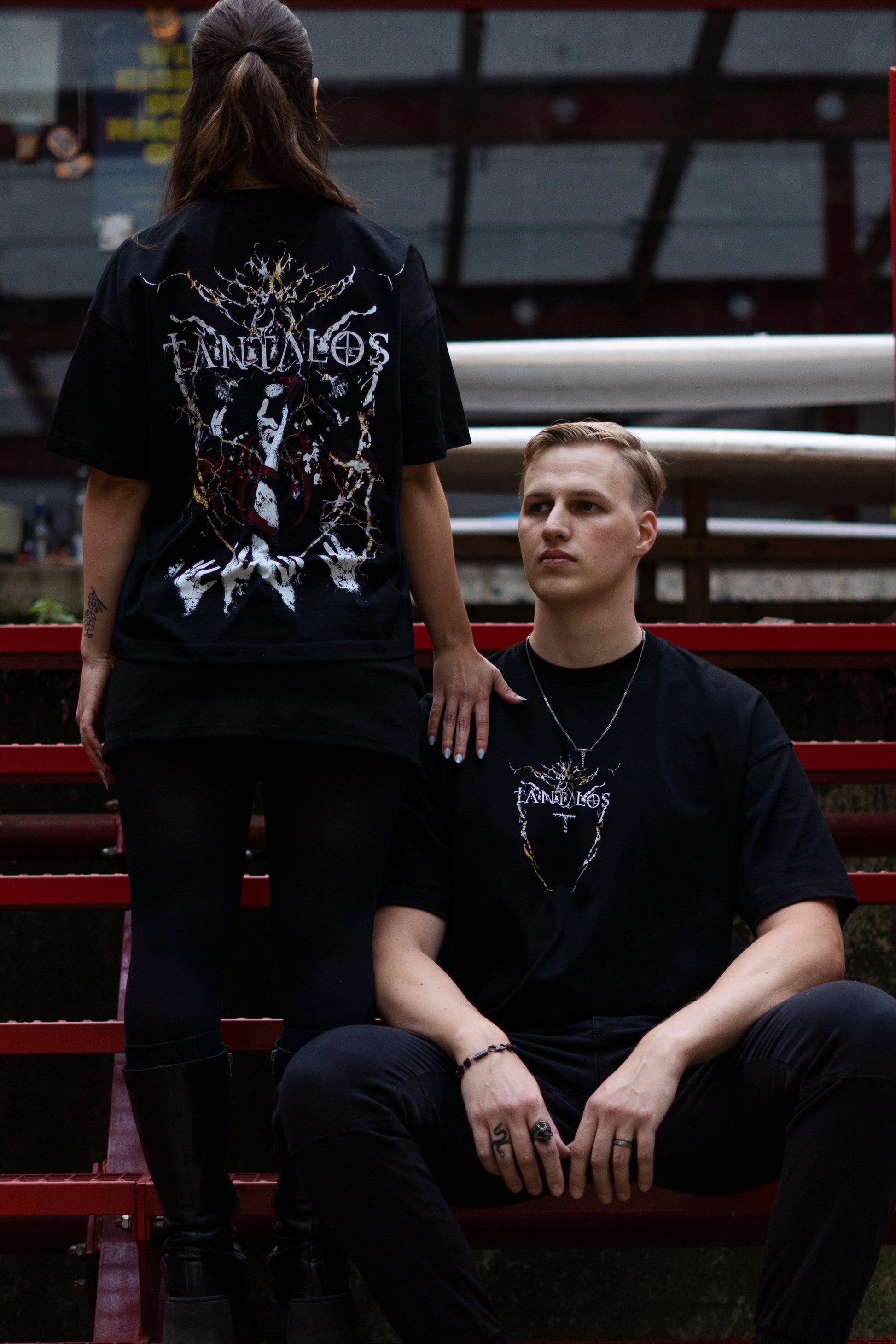 A male and a female, wearing black Techno t-shirts with white designs sitting on red metal bleachers.
