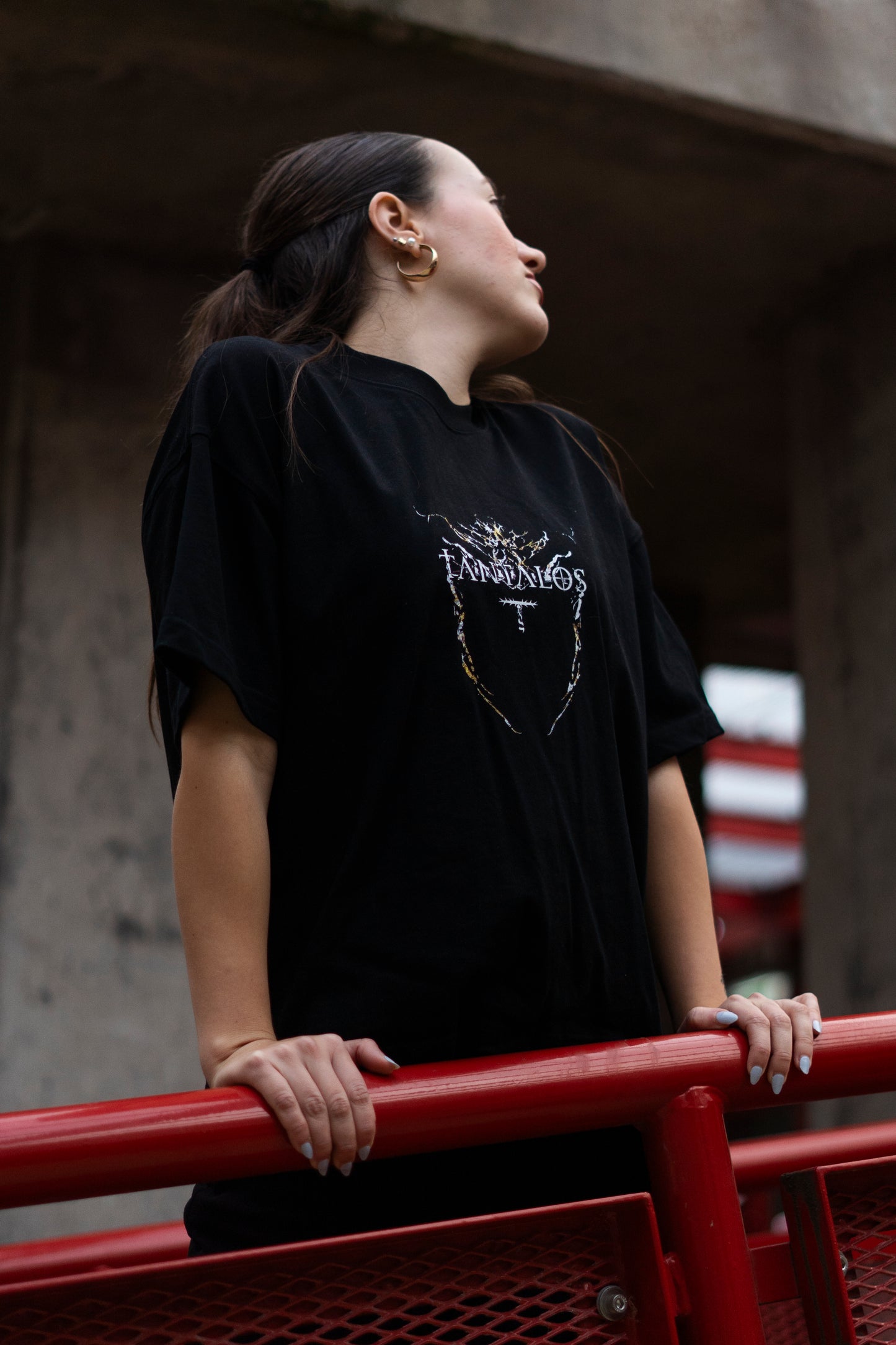 Person wearing a black techno t-shirt with a graphic design, standing against a concrete wall.